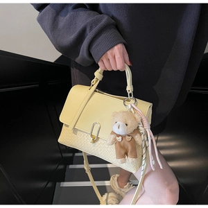 Detailansicht der gelben PU-Ledertasche mit Webstruktur, goldener Schnalle und Bärenanhänger