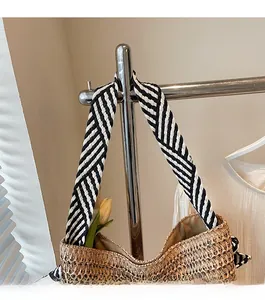 Close-up of a woven straw tote bag featuring a black and white striped wide shoulder strap