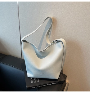 Détail d'un sac seau en cuir grainé blanc avec inscription Fashion Trend et large bandoulière