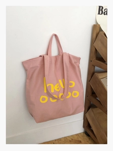 Detail van roze canvas shopper met gele hello-opdruk hangend aan een witte muur