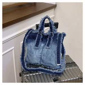 Détail du sac cabas en denim dégradé bleu avec bords effilochés sur valise