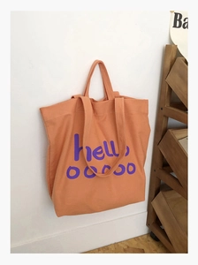 Detail van de oranje canvas shopper met paarse tekst en stevige dubbele hengsels