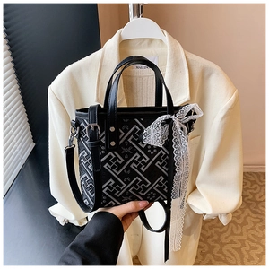 Detail of black tote bag featuring white geometric patterns and a lace bow ribbon accessory