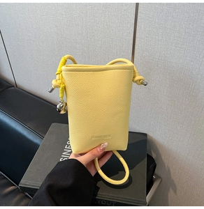 Dettaglio mini borsa gialla a tracolla in pelle con manico intrecciato e ciondolo