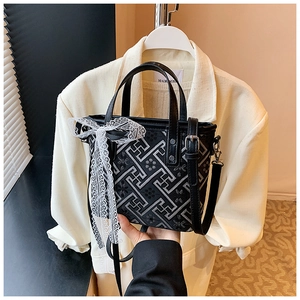 Detail of a black crossbody bucket bag with white geometric patterns and lace bow