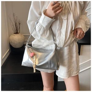 Detail of silver metallic shoulder bag with pleated texture and heart charm on white outfit