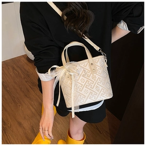 Detail of cream bucket bag with geometric embroidery and large lace bow accent