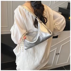 Silver hobo bag with metallic finish and braided knot charm worn as an underarm shoulder bag