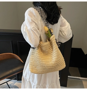 Detail of straw tote bag showing woven texture and black and white striped canvas strap