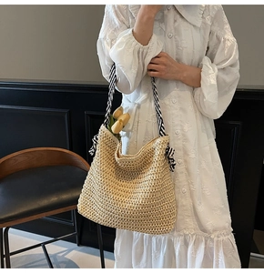 Detail of beige hollow mesh straw bag with black and white striped strap and bow