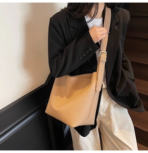 Gros plan d'un sac seau beige en cuir grainé avec bandoulière large réglable et boucle