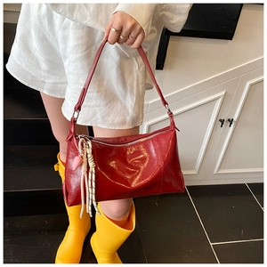 Detail of red glossy leather shoulder bag featuring a pink heart and rope charm attachment