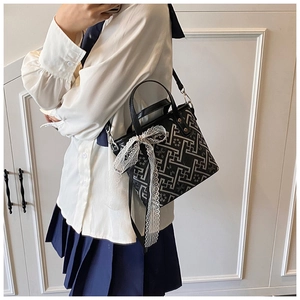 Detail of black and white geometric jacquard bucket bag with lace bow and leather strap