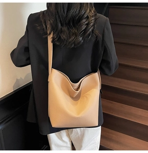 Détail du sac seau en cuir beige à motif litchi porté par un mannequin en costume