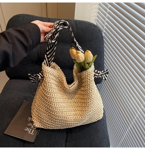Detail of beige woven straw tote bag with black and white striped ribbon handle