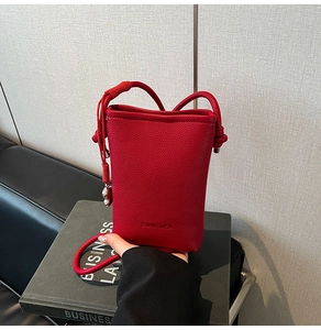 Dettaglio della borsa in pelle martellata rossa con logo impresso e ciondolo in metallo