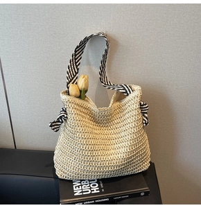 Detail view of woven straw tote bag with black and white striped handles and tulip accents