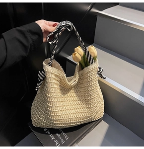 Detail of woven straw tote bag featuring black and white striped ribbon on modern stairs