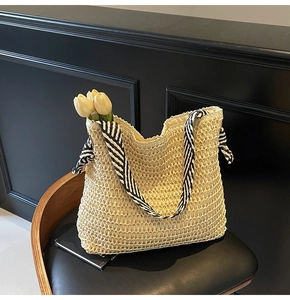 Detail of handwoven beige straw tote bag featuring black and white striped ribbon handles