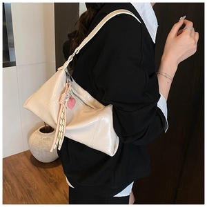 Close-up of cream patent leather Hobo bag featuring a heart charm and woven tassel details