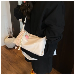 Close-up of a cream white shoulder bag with pink heart charm and woven rope detail