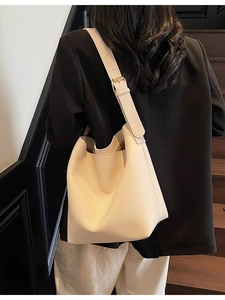 Sac seau beige en cuir grainé avec boucle dorée porté sur une veste de tailleur noire