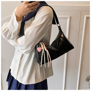 Detail of black patent leather shoulder bag with pink heart pendant and woven rope charm
