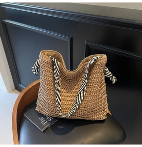 Detail of straw woven tote bag featuring khaki texture and black white striped handles