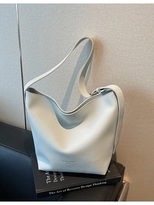 Sac seau en cuir blanc avec large bandoulière posé sur un livre noir élégant