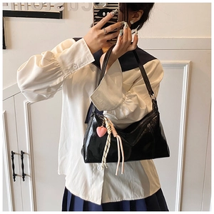 Close-up of black glossy shoulder bag with a pink heart pendant on a model in a bright room