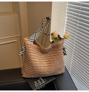 Detail of woven straw tote bag with black and white striped straps and a decorative bow