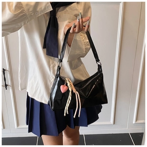 Detail of black patent leather hobo bag featuring pink heart charm and braided cord detail