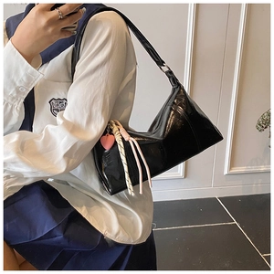 Detail of glossy black shoulder bag with a pink heart charm and woven ribbon strap