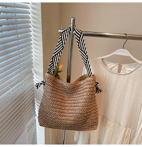 Detailed texture of straw tote bag with black and white striped canvas strap hanging