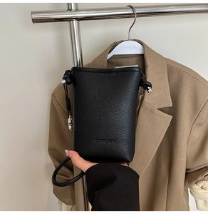 Dettaglio di una piccola borsa a secchiello nera verticale con trama a grana e ciondolo