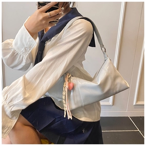 Close-up of light gray PU shoulder bag with heart charm and woven rope detail on a model