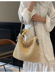Large beige straw woven tote bag with striped handles held by model in white dress