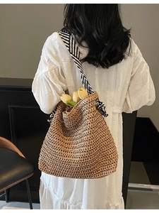 Straw shoulder tote bag with striped straps shown on a model in a resort style setting