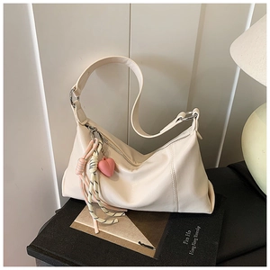 Detail of soft cream leather shoulder bag with a cute pink heart charm and woven strap accessory