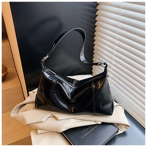 Glossy black hobo bag detail with pleated texture and metallic zipper on a soft background