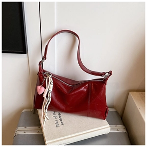 Detail of burgundy glossy leather shoulder bag with heart charm and woven strap