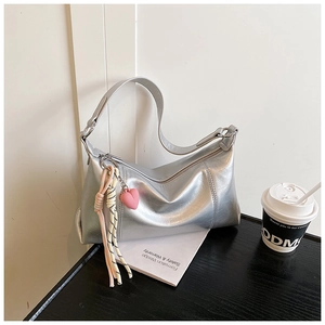 Detail of metallic silver shoulder bag featuring a pink heart charm and woven rope accent