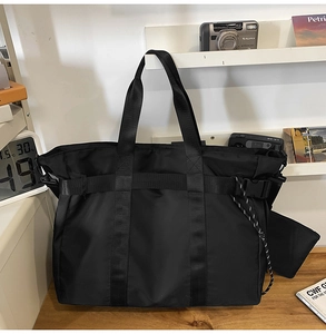Detailed view of black nylon tote bag with wide strap and buckle on a wooden desk