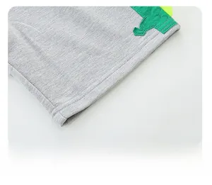 Détail du short en coton gris avec écusson dinosaure vert et pointes en feutre jaune