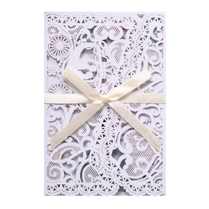 Detail of laser-cut white lace invitation with cream ribbon bow and floral inner card