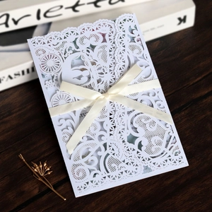 Close-up of white lace laser-cut wedding invitation with elegant satin bow