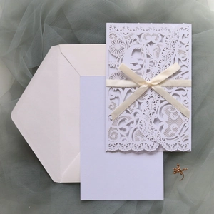 Detailed laser-cut wedding invitation with white lace patterns and an elegant silk ribbon bow
