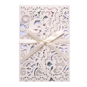 Close-up of laser-cut lace wedding invitation with elegant cream satin ribbon bow