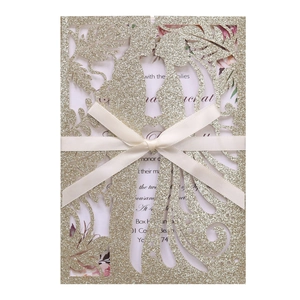 Λεπτομέρεια από χρυσό προσκλητήριο γάμου laser cut με κρεμ κορδέλα και γκλίτερ φινίρισμα