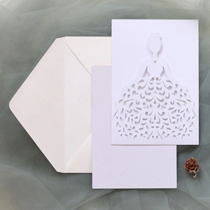 Macro shot of white laser-cut wedding invitation with bridal dress design and lilac card